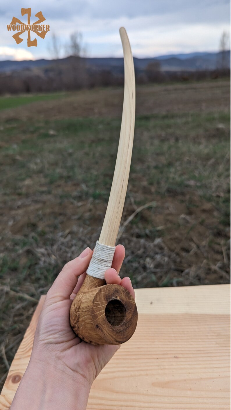 Pu&ograve; includere: Una pipa da fumo in legno con un lungo stelo curvo. La pipa &egrave; realizzata in legno marrone chiaro e ha una corda bianca avvolta attorno allo stelo vicino al fornello.