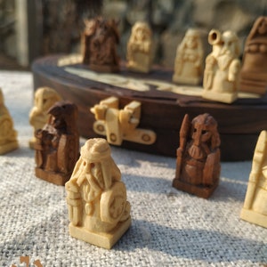 Puede incluir: Un juego de ajedrez de madera con piezas talladas intrincadamente. Las piezas son en tonos marr&oacute;n claro y oscuro, que representan figuras con detalles. El tablero de ajedrez es visible en el fondo, con un marco de madera oscura.