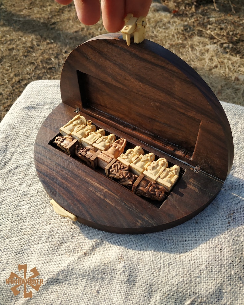 Puede incluir: Un juego de ajedrez de madera con una caja circular marr&oacute;n oscuro. Las piezas del ajedrez est&aacute;n talladas en color beige claro y se guardan en un compartimento ajustado. La tapa est&aacute; abierta, revelando las piezas del ajedrez. El juego est&aacute; sobre una superficie de color claro.