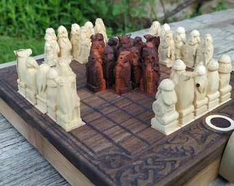 May include: A wooden chess set with intricately carved pieces. The chess board is dark brown with a carved border. The chess pieces are light and dark brown, arranged on the board, ready for play. The set is displayed outdoors.