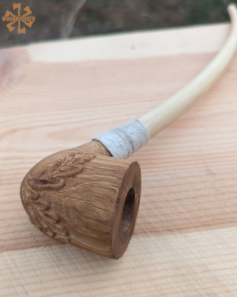 Pu&ograve; includere: Una pipa da fumo in legno con un motivo a foglia intagliato sulla ciotola e una corda bianca avvolta attorno al gambo.