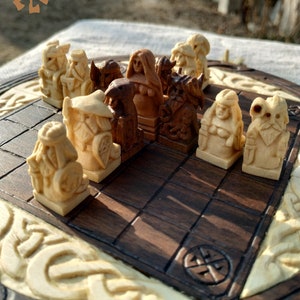 Puede incluir: Un juego de ajedrez de madera con piezas talladas en tonos de madera claros y oscuros. El tablero de ajedrez tiene una superficie de juego marr&oacute;n oscuro, un borde de madera clara y tallas decorativas. Las piezas representan figuras detalladas.