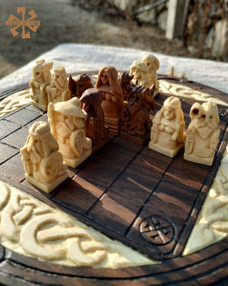 Puede incluir: Un juego de ajedrez de madera con piezas talladas en tonos de madera claros y oscuros. El tablero de ajedrez tiene una superficie de juego marr&oacute;n oscuro, un borde de madera clara y tallas decorativas. Las piezas representan figuras detalladas.