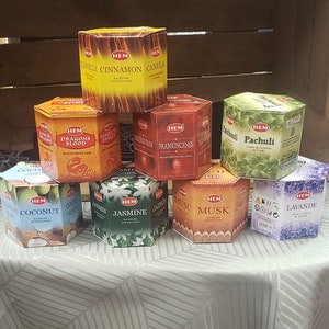 Op de afbeelding: Een assortiment HEM-wierookkegels in verschillende geuren, waaronder Drakenbloed, wierook, kokosnoot, jasmijn, musk, lavendel en patchouli. De kegels zijn verpakt in zeshoekige dozen met kleurrijke ontwerpen.