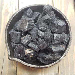 Puede incluir: Un bol lleno de cristales de turmalina negra. Los cristales son ásperos y tienen un aspecto natural y sin pulir.