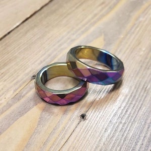 Puede incluir: Dos anillos iridiscentes con un diseño geométrico facetado. Los anillos están apilados uno encima del otro y están hechos de un metal brillante.