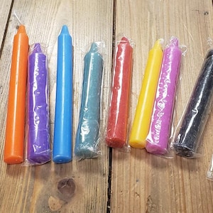 Könnte beinhalten: Sortiment von 10 kleinen, verpackten, farbigen Kerzen. Die Kerzen sind in den Farben Blau, Orange, Lila, Türkis, Rot, Gelb, Rosa, Schwarz und Weiß.