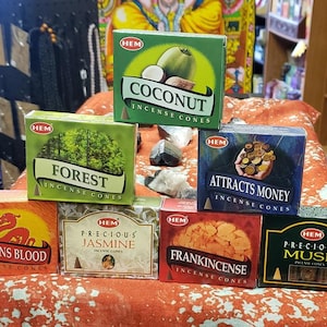 May include: Assortment of HEM incense cones in various scents, including Coconut, Forest, Dragons Blood, Precious Jasmine, Frankincense, Attracts Money, and Precious Musk. Each cone is packaged in a colorful box with the scent name and HEM logo.