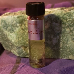 Könnte beinhalten: Eine kleine, durchsichtige Glasflasche mit schwarzem Deckel und einem silbernen Etikett mit der Aufschrift "Sweet Love". Die Flasche ist mit einer klaren Flüssigkeit gefüllt und enthält Glitzer.