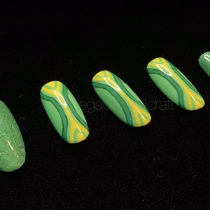 May include: Five green and yellow nail tips with a marbled design. One nail tip is solid green glitter.