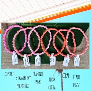 May include: Six colorful beaded bracelets with different color gradients. The bracelets are labeled with names like "Cupcake", "Strawberry Milkshake", "Flamingo Pink", "Terra Cotta", "Coral", and "Peach Fuzz".