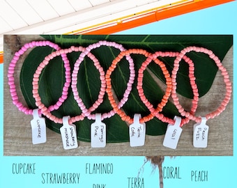 May include: Six colorful beaded bracelets with different color gradients. The bracelets are labeled with names like "Cupcake", "Strawberry Milkshake", "Flamingo Pink", "Terra Cotta", "Coral", and "Peach Fuzz".