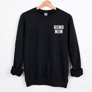 May include: Black sweatshirt with white text that reads "BOMB MOM" on the front.