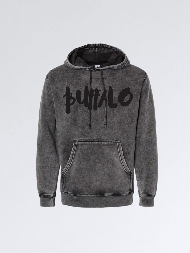 May include: A dark gray hoodie with the word "BUFFALO" in black, stylized lettering across the chest. The hoodie features a drawstring hood and a front kangaroo pocket. The fabric has a textured, acid wash appearance.