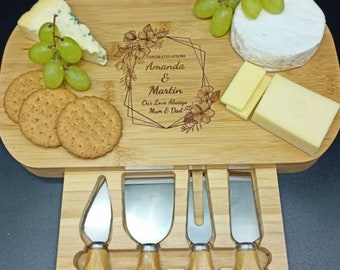 Könnte beinhalten: Ein Käseboard aus Holz mit einer Schublade, die vier Käsemesser enthält. Das Brett ist mit dem Text "Congratulations Amanda & Martin Our Love Always Mum & Dad" und einem floralen Design graviert. Das Brett ist mit Käse, Crackern und Trauben gefüllt.