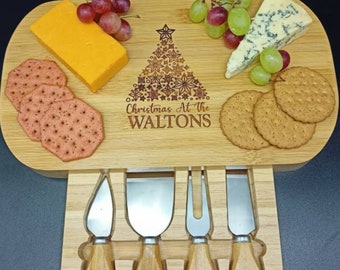 May include: A wooden cheese board with a Christmas tree design and the text "Christmas At The WALTONS". The board holds cheese, crackers, and grapes. Four cheese knives are stored in a drawer below.