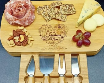 May include: A wooden cheese board with a built-in drawer for cheese knives. The board is engraved with the words "Merry Christmas Mum" and "Love from Julie & Peter". The board is filled with various snacks, including cheese, crackers, grapes, nuts, and salami.