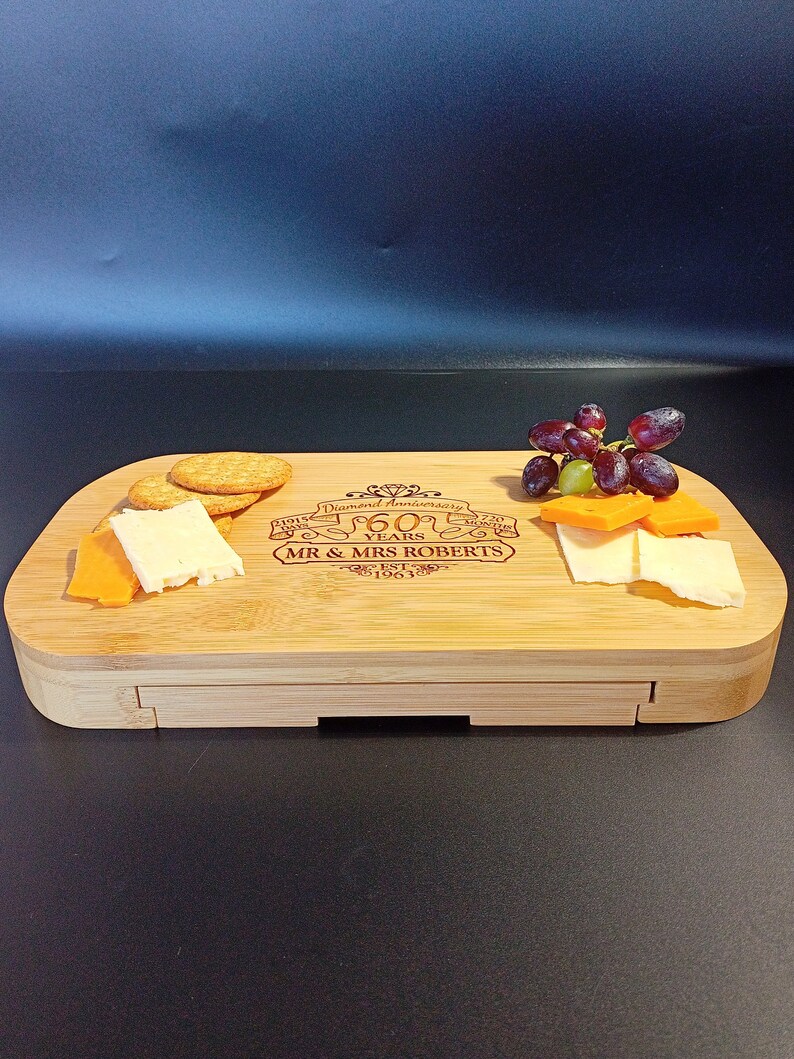 May include: A bamboo cheese board with a drawer for storing crackers. The board is engraved with "Diamond Anniversary 60 Years" and "Mr. & Mrs. Roberts Est. 1963".