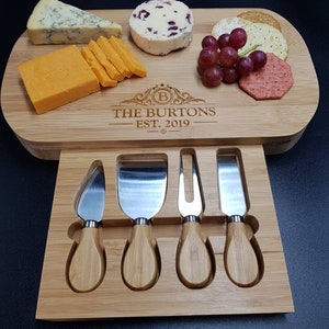 Peut inclure: Un plateau &agrave; fromage en bois avec un tiroir pour les couteaux &agrave; fromage. Le plateau porte une inscription personnalis&eacute;e qui dit "The Burtons Est. 2019". Le plateau est rempli de fromage, de craquelins, de raisins et d'une boule de fromage aux canneberges.