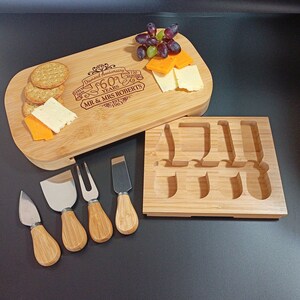 May include: A bamboo cheese board with a knife holder and five cheese knives. The board is engraved with "Diamond Anniversary 60 Years Mr. & Mrs. Roberts Est. 1963".