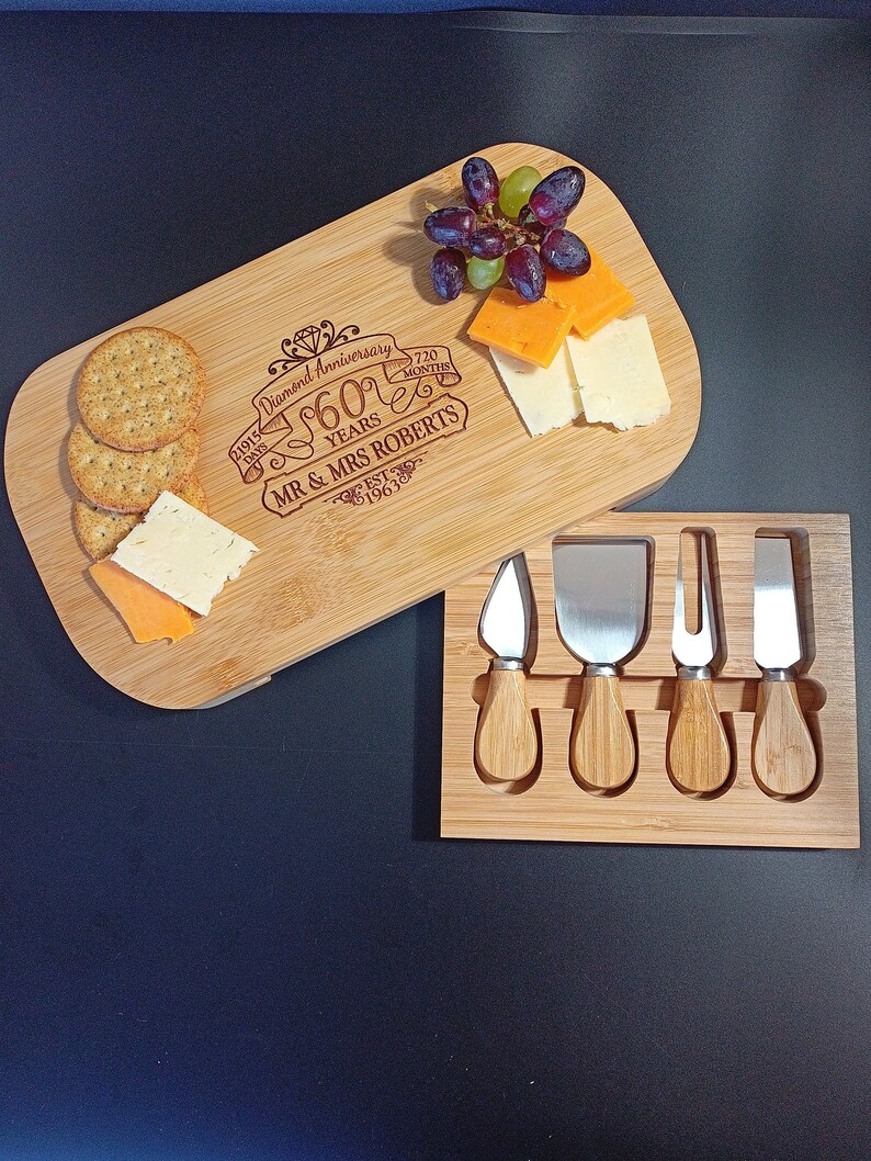 May include: A wooden cheese board with a personalized inscription celebrating a 60th anniversary. The inscription reads "Diamond Anniversary 60 Years 720 Months Mr & Mrs Roberts Est 1963". The board includes a set of four cheese knives with wooden handles.