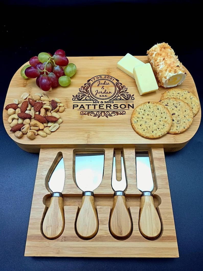 Peut inclure: Un plateau &agrave; fromage en bois avec une inscription personnalis&eacute;e pour un mariage. L'inscription est "17.05.2021 Jodie & Jordan xxx MR & MRS PATERSON". Le plateau a un tiroir int&eacute;gr&eacute; avec quatre couteaux &agrave; fromage.