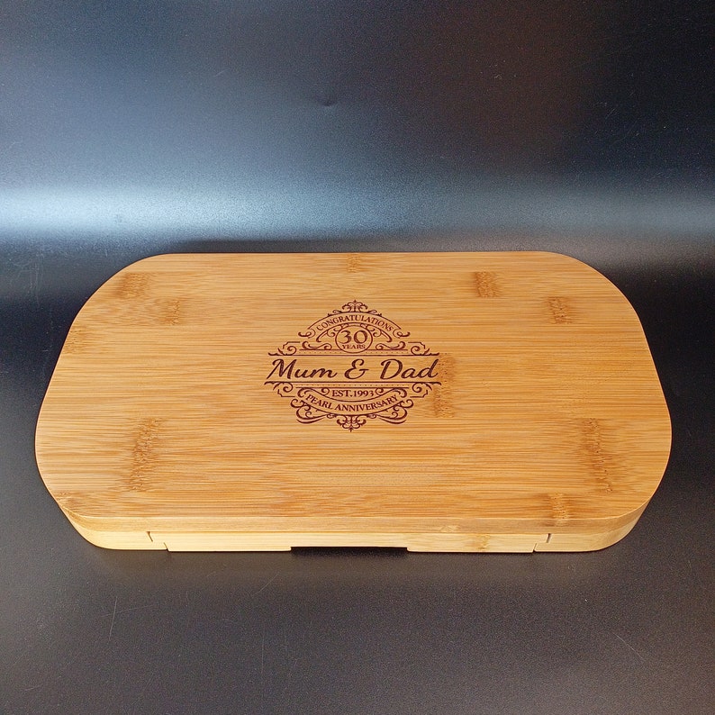 May include: A rectangular wooden serving tray with a raised edge and a hinged lid. The tray is made of light brown bamboo and has a dark brown engraved design that says "Congratulations 30 Years Mum & Dad Est. 1991 Pearl Anniversary".