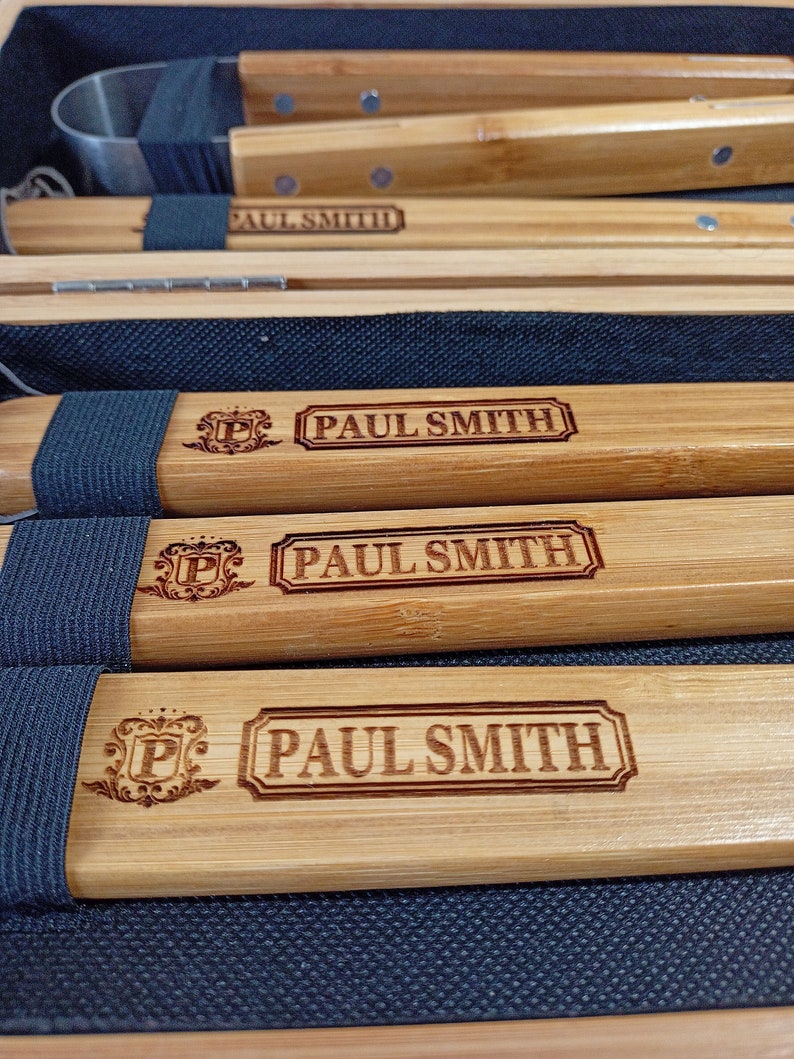 Puede incluir: Cuatro herramientas de parrilla de madera con correas negras y un logotipo de Paul Smith. Las herramientas est&aacute;n en una caja de madera con un forro de tela negro.