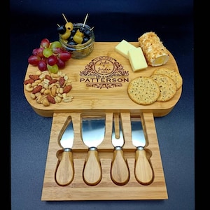 Peut inclure: Un plateau &agrave; fromage en bois avec un porte-couteaux int&eacute;gr&eacute;. Le plateau est grav&eacute; avec la date "17.05.2021", les noms "Jodie & Jordan", et le texte "Mr & Mrs Patterson". Le plateau est rempli de collations, notamment des raisins, des olives, des noix, du fromage et des craquelins.