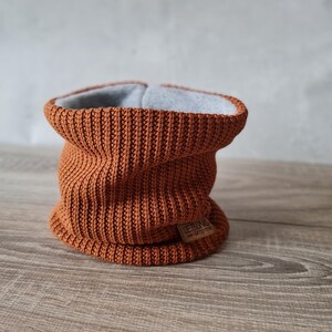 Könnte beinhalten: Ein brauner gestrickter Halsschmuck mit grauem Fleecefutter. Der Halsschmuck hat ein braunes Leder-Etikett mit dem Wort "LEGENDS" und dem Text "GÖTEBORG" darauf.
