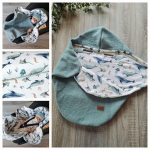Peut inclure: Une couverture de siège auto pour bébé de couleur sarcelle, avec un motif de baleines et de créatures marines à l'intérieur. La couverture est faite d'une matière douce et est conçue pour garder un bébé au chaud et à l'aise.