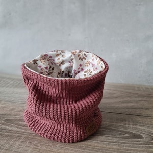 Peut inclure: Un tour de cou en tricot rose avec une doublure à imprimé floral. Le tour de cou a une étiquette en cuir marron avec le texte "LEBUNG" dessus.