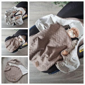 Peut inclure: Une couverture de siège auto pour bébé avec un extérieur matelassé texturé marron et un intérieur blanc à motifs. La couverture est enroulée autour d'une poupée, avec une capuche assortie. Le siège auto est noir.