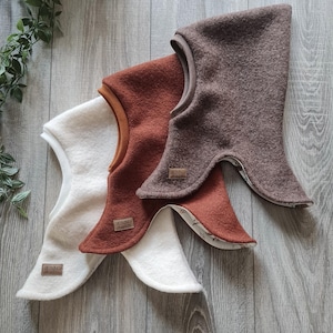 Peut inclure: Trois balaclavas en polaire de différentes couleurs : marron, rouille et blanc. Chaque balaclava porte une étiquette marron avec le texte "Le Blanc".