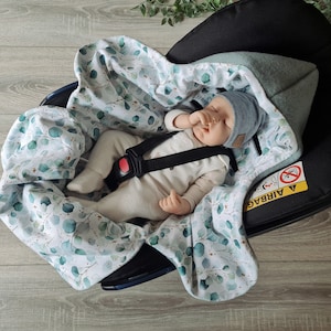 Pu&ograve; includere: Un bambino dorme in un seggiolino auto con una coperta bianca e verde con stampa di eucalipto. Il seggiolino auto ha un'etichetta di avvertenza "Airbag" nera e gialla.