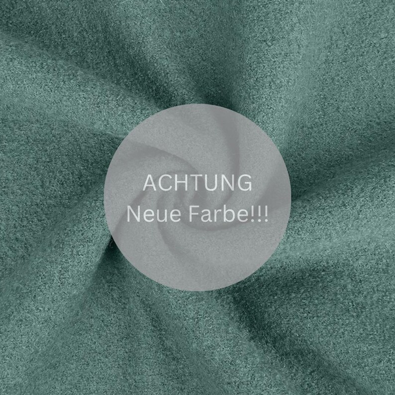 Pu&ograve; includere: Primo piano di un tessuto morbido di colore verde con un cerchio bianco al centro. Il cerchio contiene il testo "ACHTUNG Neue Farbe!!!" in nero.