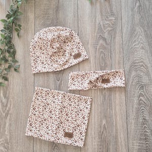 Könnte beinhalten: Ein Set aus drei braunen und weißen Accessoires aus Leopardenstoff. Das Set beinhaltet eine Mütze, ein Stirnband und einen Halsschmeichler. Jedes Teil hat ein braunes Leder-Etikett mit dem aufgedruckten Wort "ESPRIT".