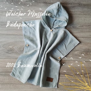 Könnte beinhalten: Ein hellblaues Kapuzenhandtuch aus 100% Baumwollmusselin. Das Handtuch hat ein "Weicher Musselin Badeponcho" Etikett und ein "Handmade with Love" Etikett.
