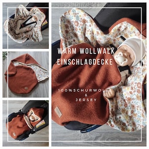 Könnte beinhalten: Eine rostfarbene Babydecke mit floralem Innenfutter, in mehreren Ansichten gezeigt. Die Decke ist um ein Baby in einem Autositz gewickelt und wird auch offen gezeigt. Auf der Decke steht "WARM WOLLWALK EINSCHLAGDECKE" und "100% SCHURWOLLE & JERSEY."