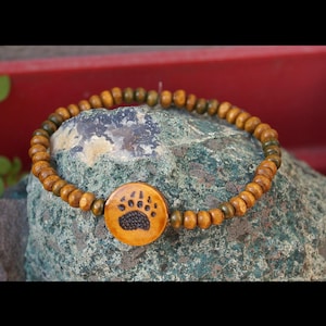 May include: A wooden bracelet with brown and green beads and a brown bear paw charm.