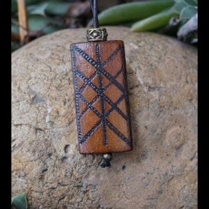 Può includere: Un ciondolo in legno con un design geometrico nero e marrone. Il ciondolo è su un cordoncino in pelle marrone con una perla in ottone.