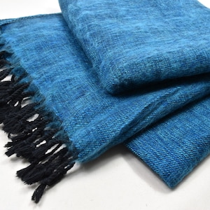 Puede incluir: Una manta suave de color azul con flecos negros. La manta está doblada por la mitad y los flecos son visibles en ambos lados.