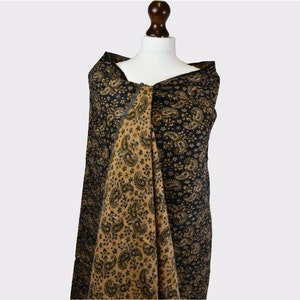 May include: A black and gold paisley patterned shawl draped over a mannequin.