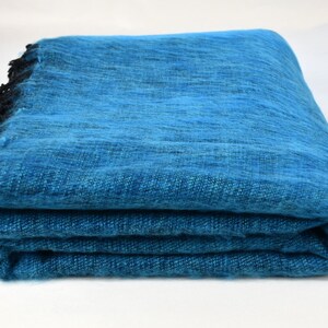 May include: A folded teal blue pashmina shawl with black fringe trim.