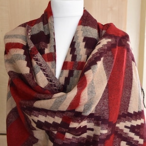 May include: A red, beige, and burgundy plaid scarf with a geometric pattern. The scarf is draped over a mannequin.