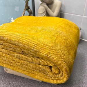 Pode incluir: Um cobertor amarelo mostarda dobrado com uma trama texturizada. O cobertor está bem enrolado, mostrando seu material espesso e macio. O cobertor é de uma cor quente e convidativa, perfeito para decoração de casa.