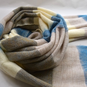 May include: A soft, striped scarf in shades of cream, blue, and brown. The scarf is made of a lightweight, breathable fabric and is perfect for layering in the cooler months.