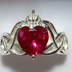 Puede incluir: Un anillo de plata con un diseño de nudo celta y una gran piedra preciosa en forma de corazón de rubí.