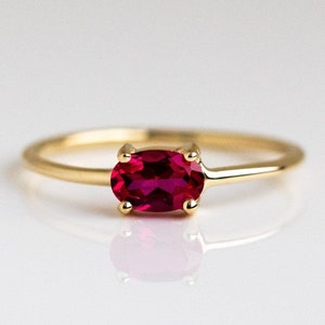 Puede incluir: Un anillo de oro con una vibrante gema de rubí de corte ovalado. El rubí es de un color rojo intenso, engastado en una montura de cuatro garras. La banda es delgada y de oro pulido. Una joya clásica y elegante.