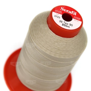 May include: A spool of Serafil thread in a light beige color. The spool has a red top with the text "Serafil" and "30 Tex 90 900m". The thread is tightly wound around the spool, which sits on a red base.